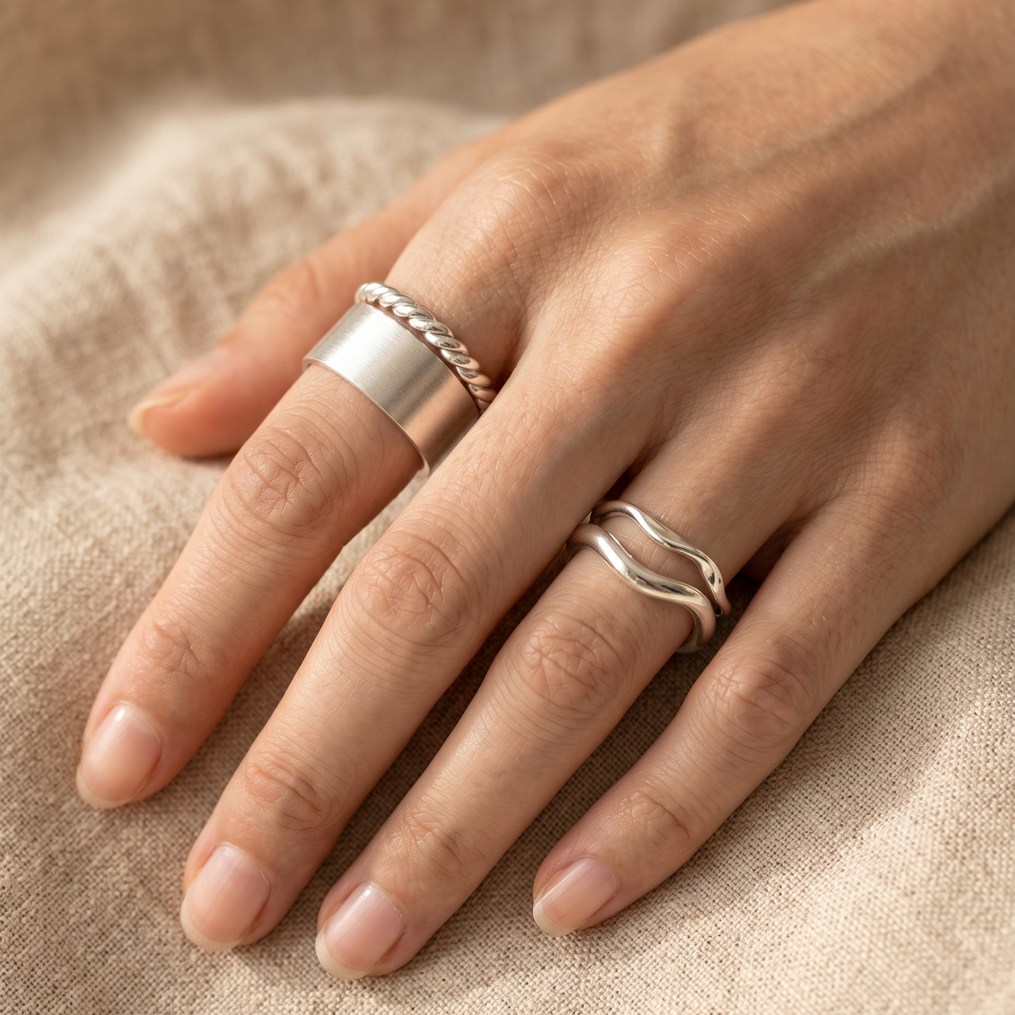 Hand mit drei gestackten Silberringen